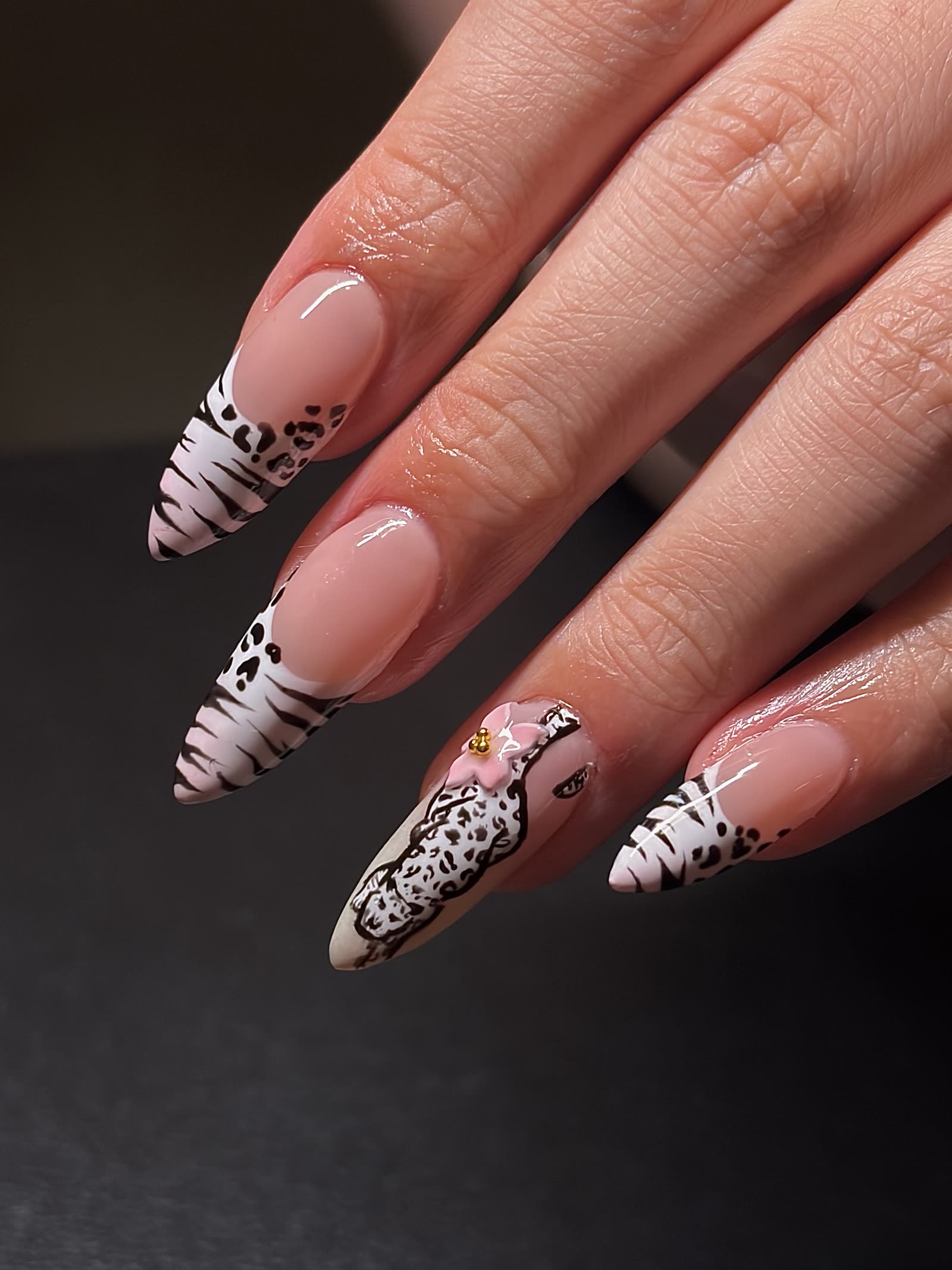 Nude nails with black-and-white zebra and leopard French tips, one accent nail carrying a 3D pink flower