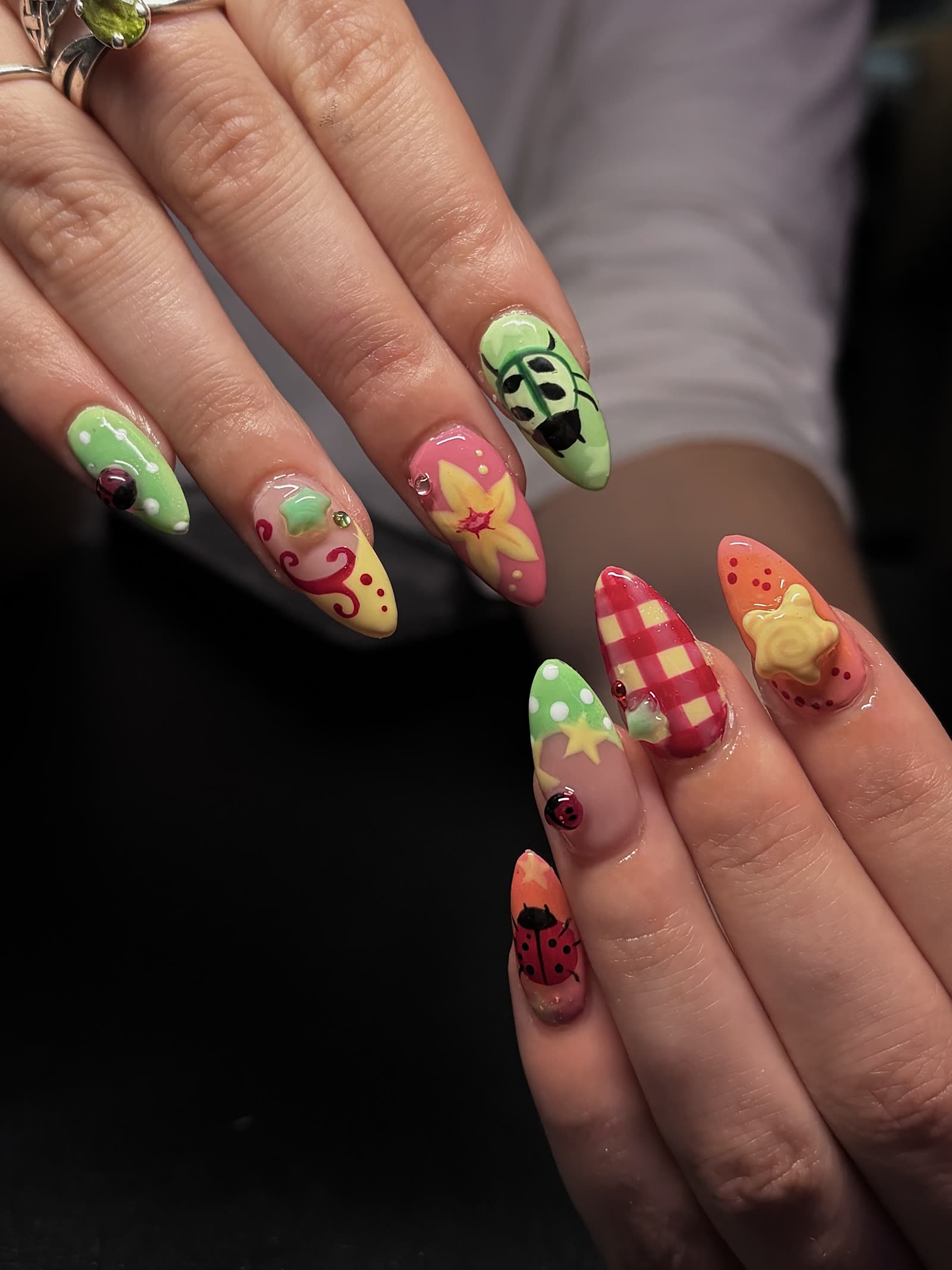Bright novelty set — a green beetle, red gingham, a yellow flower and polka dots across almond nails