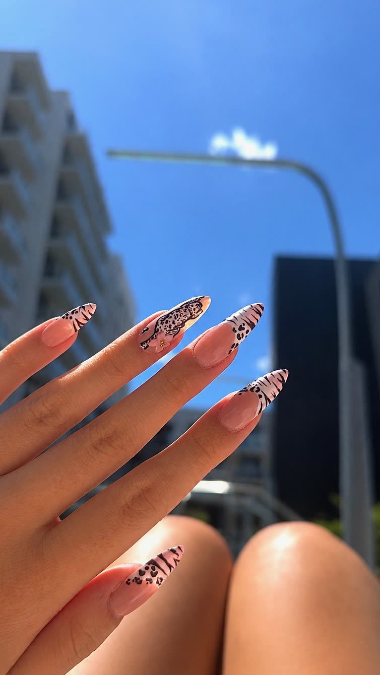Zebra and leopard French tips on almond nails, photographed against a blue sky