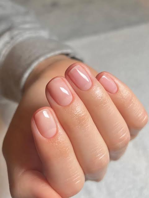 Short, glossy sheer-pink nails on a relaxed hand